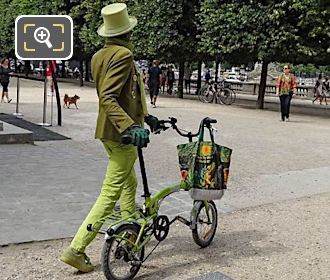 Man in green top hat, jacket, glasses and gloves with green bike in Tuileries Gardens