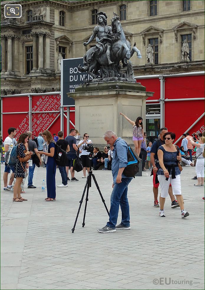Photographer with camera on tripod taking pictures of The Louvre